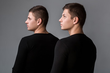 The two twin brother stand with their backs on the gray backgrou