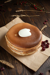 a pile of pancakes, berries, cookies, sour cream and a cutting board on parchment on a dark wooden table