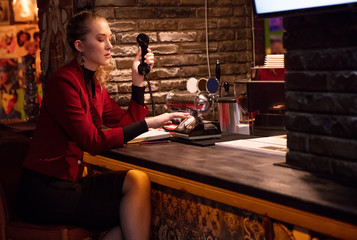 blonde in  burgundy style suit 80s dials  number on retro phone on bar counter