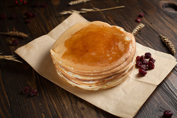 a pile of pancakes, berries, cookies, butter and a cutting board on parchment on a dark wooden table