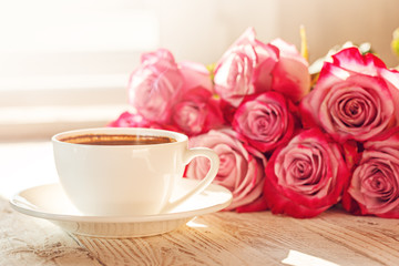 White cup of coffee for valentine or romantic morning with pink roses.