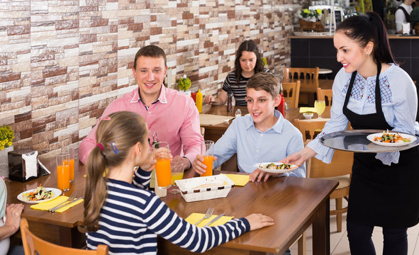 Polite charming waitress bringing ordered dishes to family