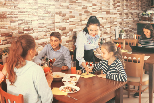courteous brunette waitress serving family in family cafe