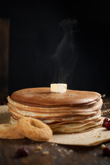 a pile of pancakes, berries, cookies, butter and a cutting board on parchment on a dark wooden table