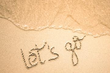 Let's Go word is written on the beach sand