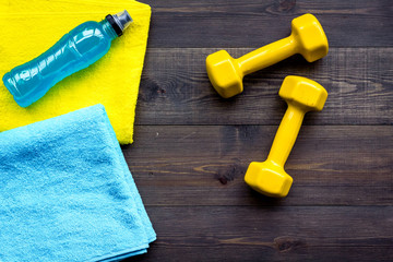 Fitness equipment. Dumbbells, water, expander on dark wooden background top view