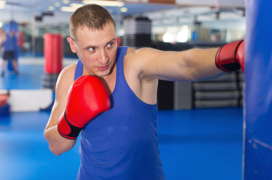 Active male is training with punching bag in box gym