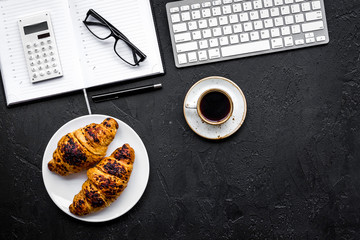 Morning of businessman. Coffee and croissants for breakfast near keyboard and notebook. Black background top view copy space