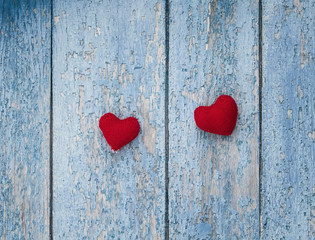 two bright red heart made of yarn on a background of wooden walls with a shabby old blue paint stripes