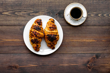 Light breakfast. Small cup of black coffee and croissant on dark wooden background top view copy space