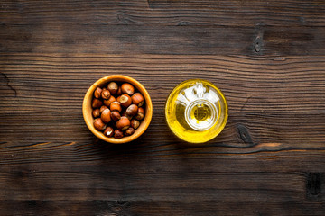 Oil as cosmetics. Haselnut oil near nut in shell on dark wooden background top view copy space