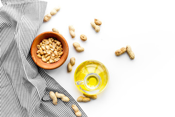 Oil for skin care. Peanut oil i n jar near peanut in shell in bowl on white background top view copy space
