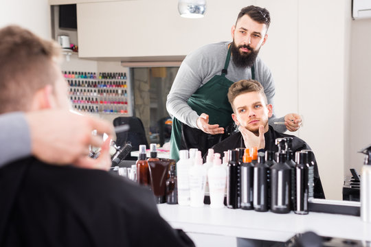 thoughtful guy stylist creating haircut for man client at hairdressing salon