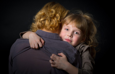 Photo shooting indoors. On a black background. Child ( girl ) hugs his mother.
