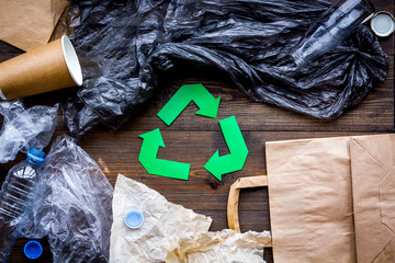 Green paper recycling sign among waste materials paper, plastic, polyethylene on dark wooden...