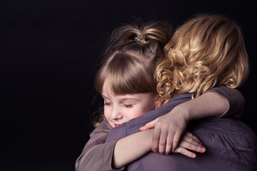 Fototapeta na wymiar Photo shooting indoors. On a black background. Child ( girl ) hugs his mother. 
