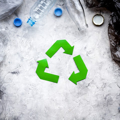Green paper recycling sign among waste polyethylene bags and plastic bottles on grey stone background top view copy space