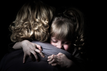 Photo shooting indoors. On a black background. Child ( girl ) hugs his mother.
