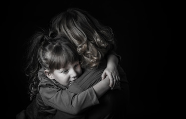 Photo shooting indoors. On a black background. Child ( girl ) hugs his mother.
