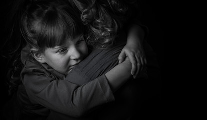 Photo shooting indoors. On a black background. Child ( girl ) hugs his mother.
