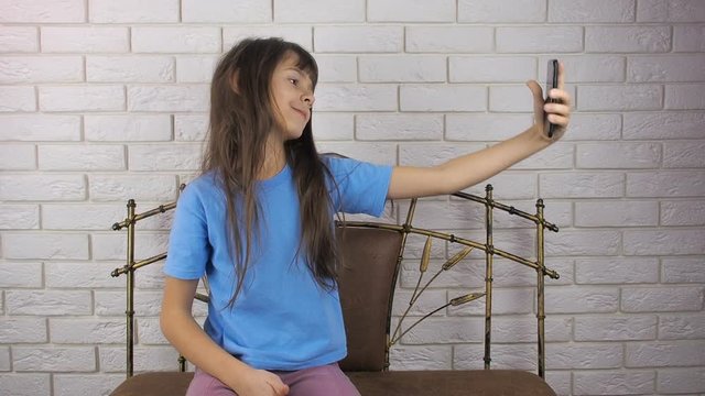 The child is playing with the phone. A beautiful little girl takes pictures of herself with a phone.