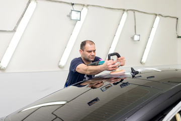 A man polishes a black car with a polisher