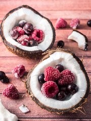 Coconut halves with Frozen Berries on a dark wooden background.