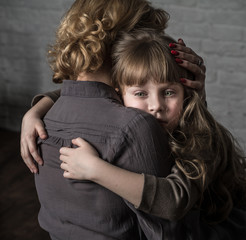 Photo shooting indoors. On the background of a white brick wall . Child ( girl ) hugs his mother.
