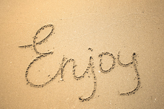 Enjoy word is written on the beach sand