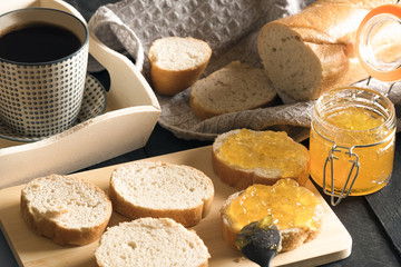 Sliced french bread with peach jam and coffee - Breakfast with french bread, sliced on a wooden cutting board, and smeared with homemade peach jam and a cup of hot coffee on a white wooden tray. 