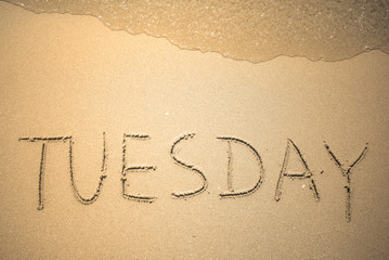Tuesday word is written on the beach sand