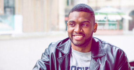 Handsome african american young man smiling - Close-up portrait of black attractive male in confident attitude looking aside  sitting inside cafe bar- Dark cinematic filter