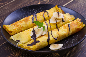 Home-made pancakes  filled with sweet white cheese, served with bananas, chocolate and mint. Wrapped pancakes