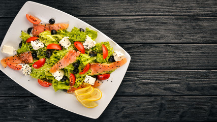 Salmon salad, feta cheese, salad leaves and fresh vegetables on the plate. On a wooden background. Top view. Free space for text.