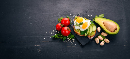 Avocado sandwich with quail eggs, cucumber and pistachios. On a wooden background. Top view. Free space for your text.