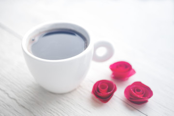 Cup of hot coffee and decorative red flowers on a white wooden surface of a table. Romantic background