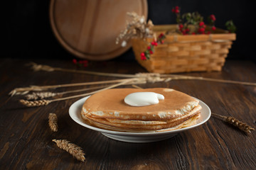 a pile of pancakes, berries, cookies, sour cream and a cutting board on parchment on a dark wooden table