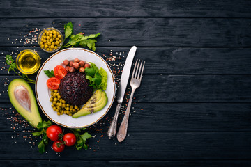 Healthy food. Black rice, avocado, cherry tomatoes, green peas and hazelnut. On a wooden background. Top view. Free space for your text.