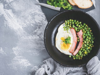 Appetizing ribs with green peas and fried eggs, sprinkled with cilantro, cooked on a vintage, cast-iron frying pan