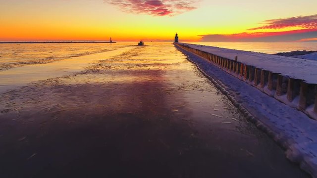Lake Michigan fishing boat going out past Lighthouse in colorful predawn twilight, on a January morning, aerial view.