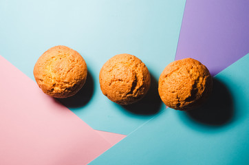 three cupcakes. bakery products. confectionery. view from above. background of three colors, pink, sky blue, violet