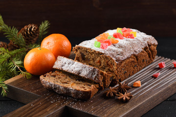 Traditional homemade chocolate fruit cake decorated with candied fruits, clementines, star anise and fir branch on carved dark oak board