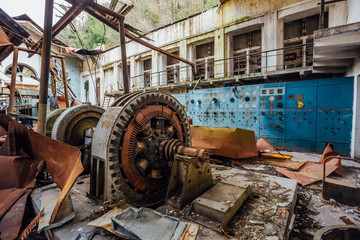 Ruined abandoned electrical substation. Rusty generator at machinery. Demolished roof