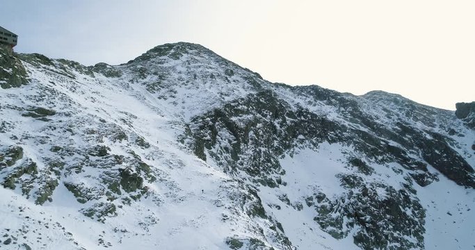 Backward aerial over winter snowy mountain with mountaineering skier people walking up climbing.snow covered mountains top ice glacier.Winter wild nature outdoor establisher.4k drone flight