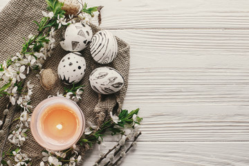 happy easter greeting card. modern easter eggs on rustic white wooden background with fresh spring flowers and candle top view. space for text. stylish painted eggs flat lay