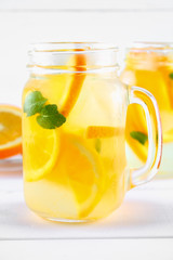 Orange detox water in mason jars on a white wooden table. Healthy food, drinks.