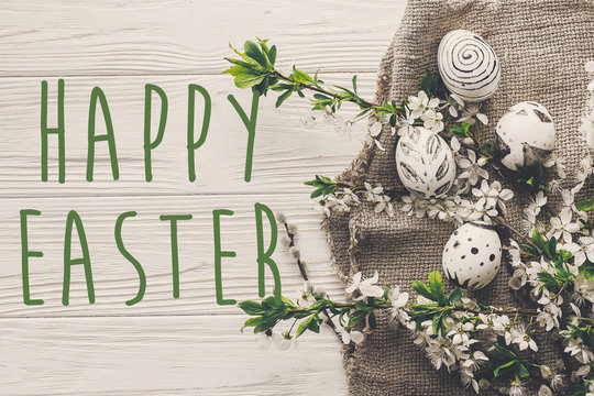 happy easter text flat lay with flowers and stylish eggs on rustic wooden background top view. modern green easter greeting card. space for text