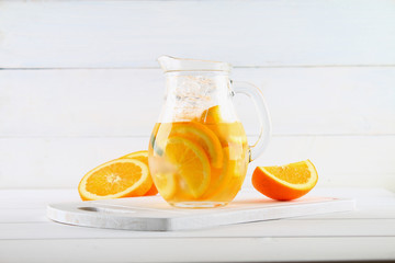 Orange detox water in a jug on a white wooden table. Healthy food, drinks.
