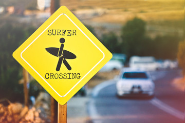 Surfer crossing,  yellow road sign on the road to the beach.