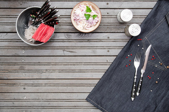 Serving background on dark grey metal background with space for text. Top view Knife and fork wrapped on a denim napkin, cutlery, cole slaw salad, pepper salt shaker